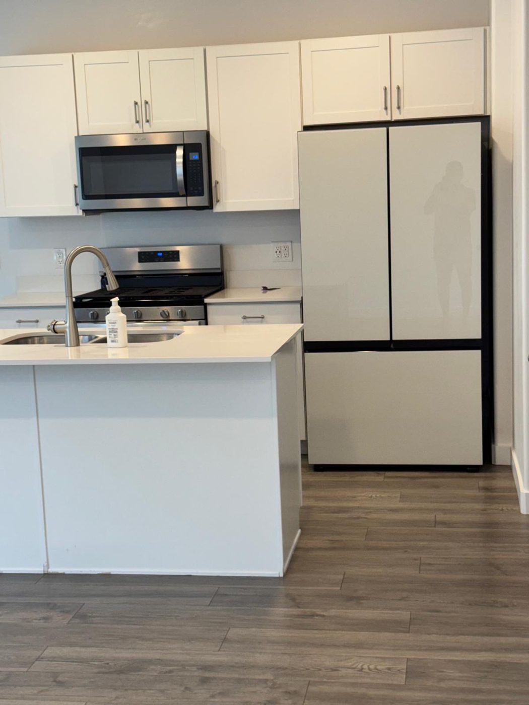 Freshly cleaned kitchen with white cabinets, stainless microwave, range, and a spotless quartz island after cleaning by Alkate Cleaning Services
