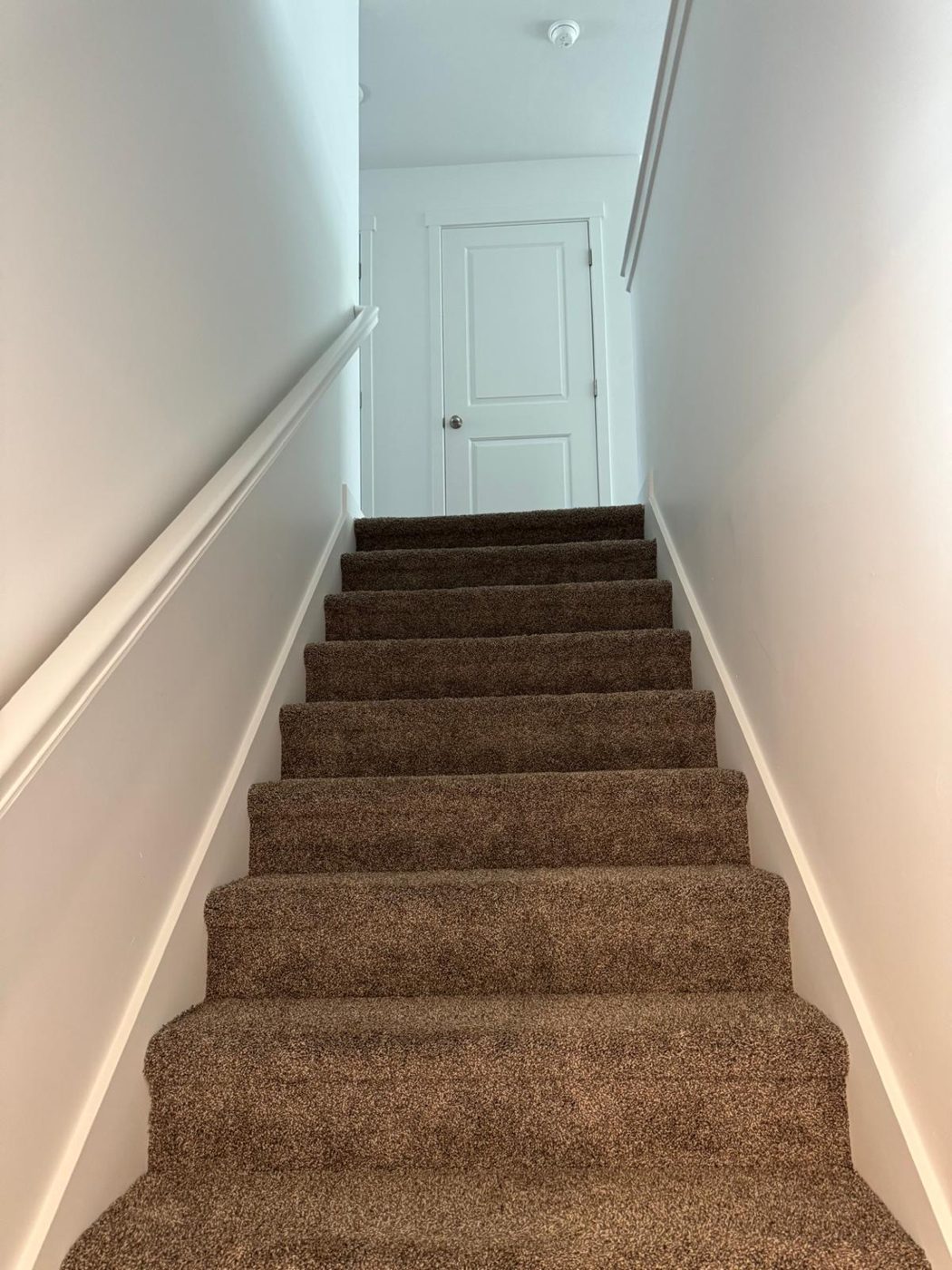 Vacuumed carpeted staircase and hallway with clean white walls and trim after a move-out cleaning