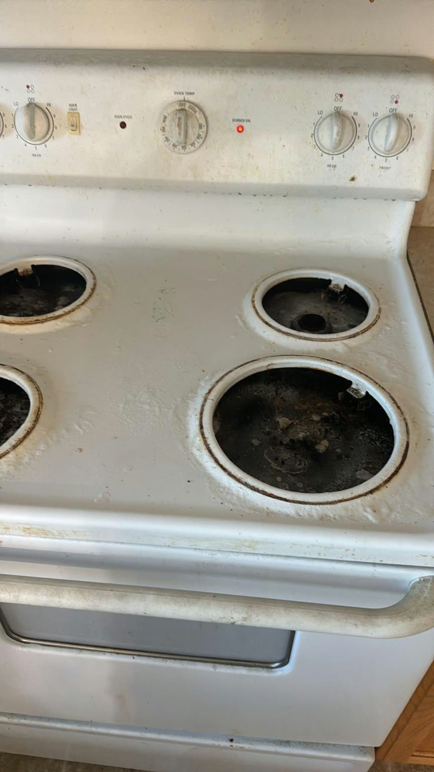 White electric stove top before cleaning, with burnt-on food, rust rings around the burners, and a soiled control panel