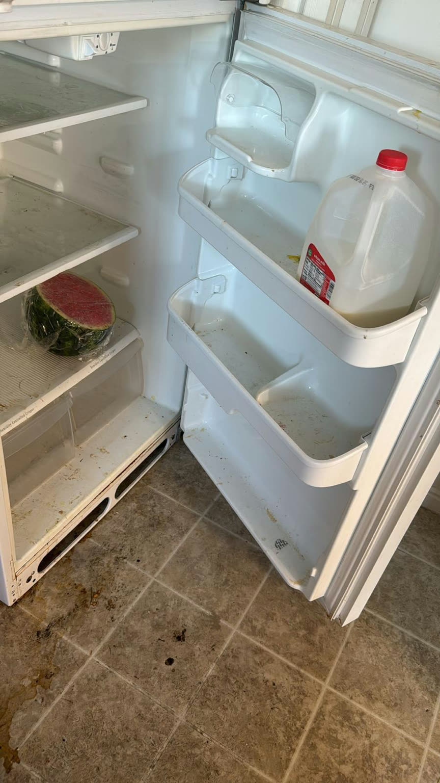 Full refrigerator interior before cleaning, with a watermelon and milk container, food spills, and sticky residue on the shelves and door bins